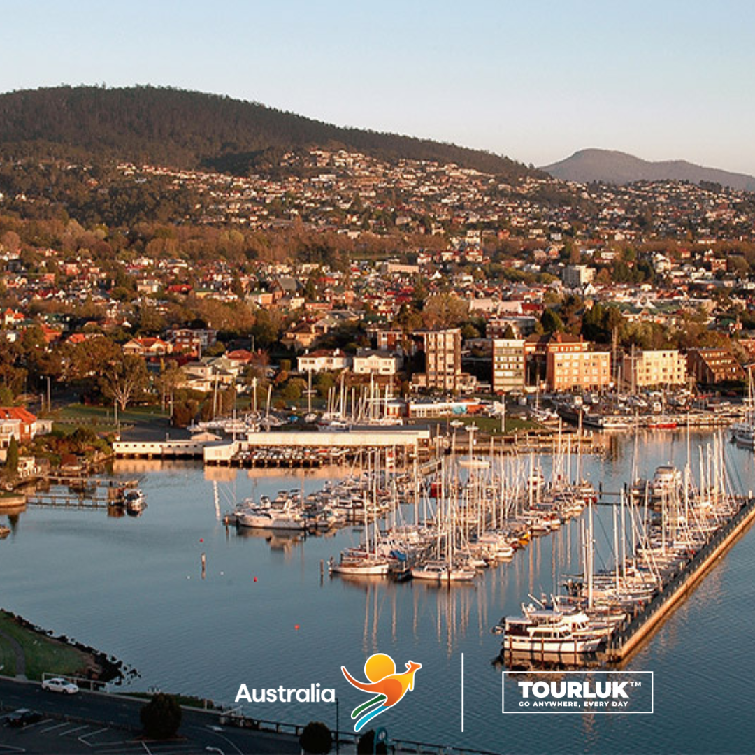Toàn cảnh thành phố Hobart, Tasmania với bến cảng nhộn nhịp, những chiếc thuyền neo đậu và khu dân cư trải dài dưới chân núi, tạo nên khung cảnh yên bình và đặc trưng của thành phố cảng lâu đời tại Úc.