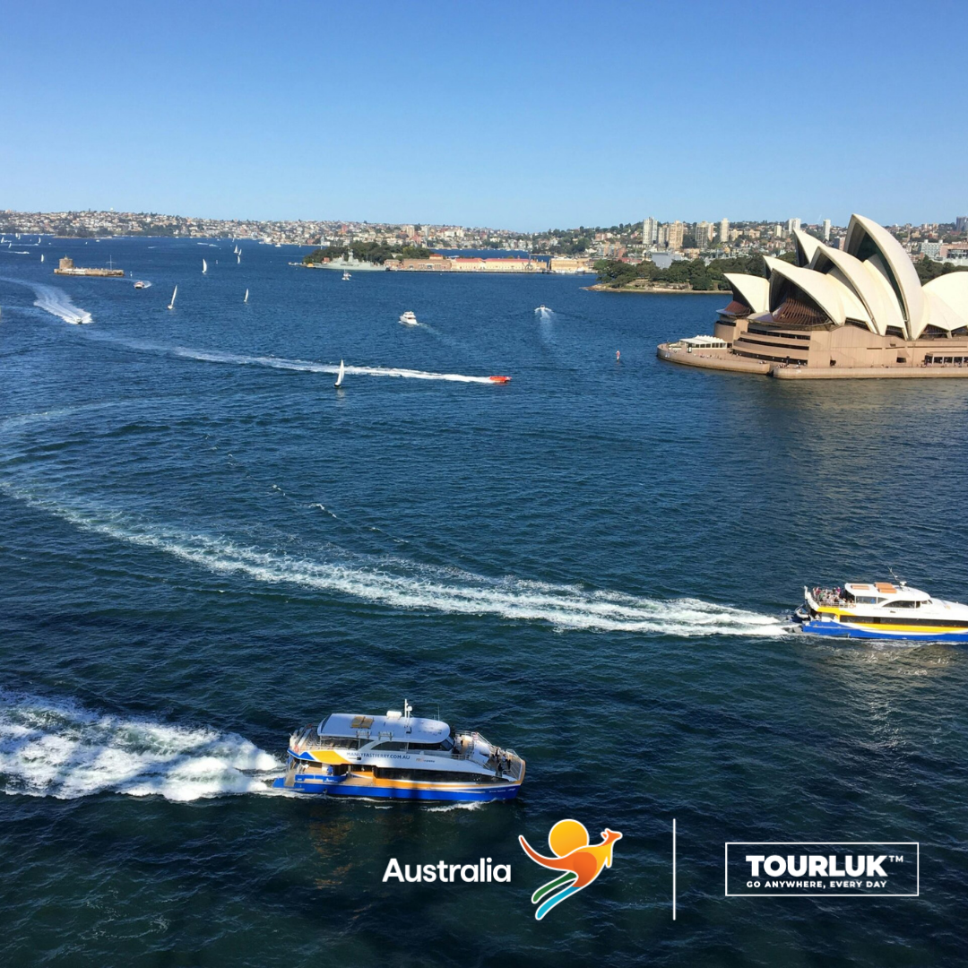 Toàn cảnh cảng Sydney, Australia với Nhà hát Opera Sydney bên bờ biển, nhiều tàu cao tốc di chuyển trên mặt nước xanh dưới bầu trời trong xanh.