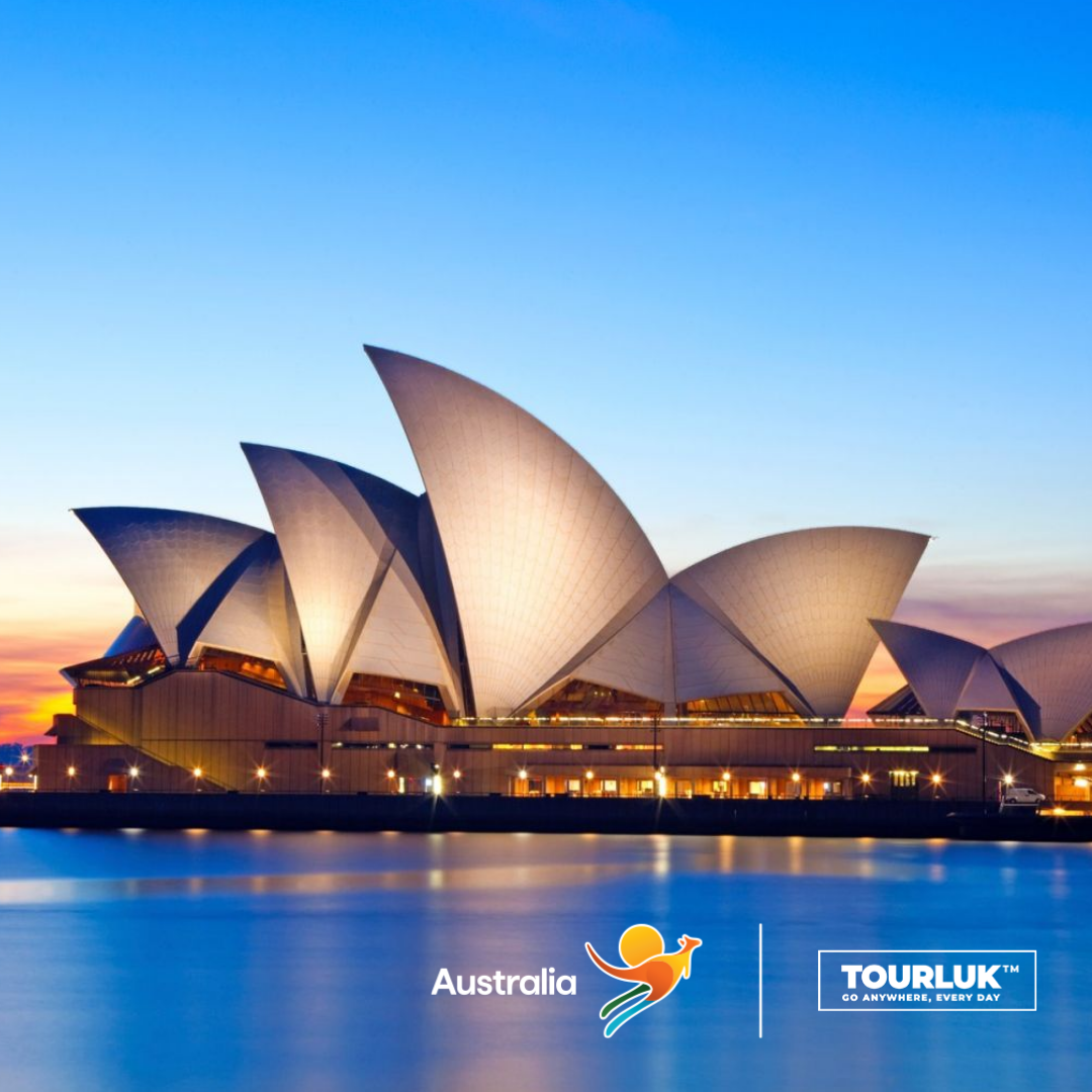 Nhà hát Opera Sydney nổi bật bên bờ cảng lúc hoàng hôn, với kiến trúc mái vòm độc đáo phản chiếu trên mặt nước yên ả