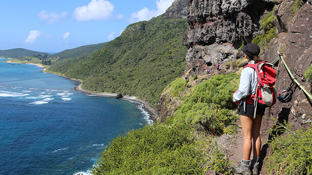 Du khách đang trekking trên vách núi tại Lord Howe Island, Úc, với góc nhìn toàn cảnh đại dương xanh sâu và bờ biển uốn lượn, mang đến trải nghiệm khám phá thiên nhiên hoang sơ và hùng vĩ.