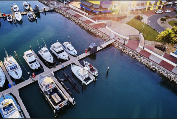 Bến du thuyền với nhiều tàu neo đậu cạnh cầu cảng, nhìn từ trên cao bên bờ kè và khu dân cư ven biển